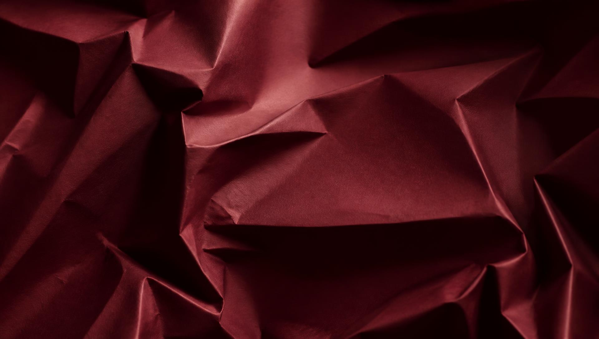 Creased maroon paper lit by raking light