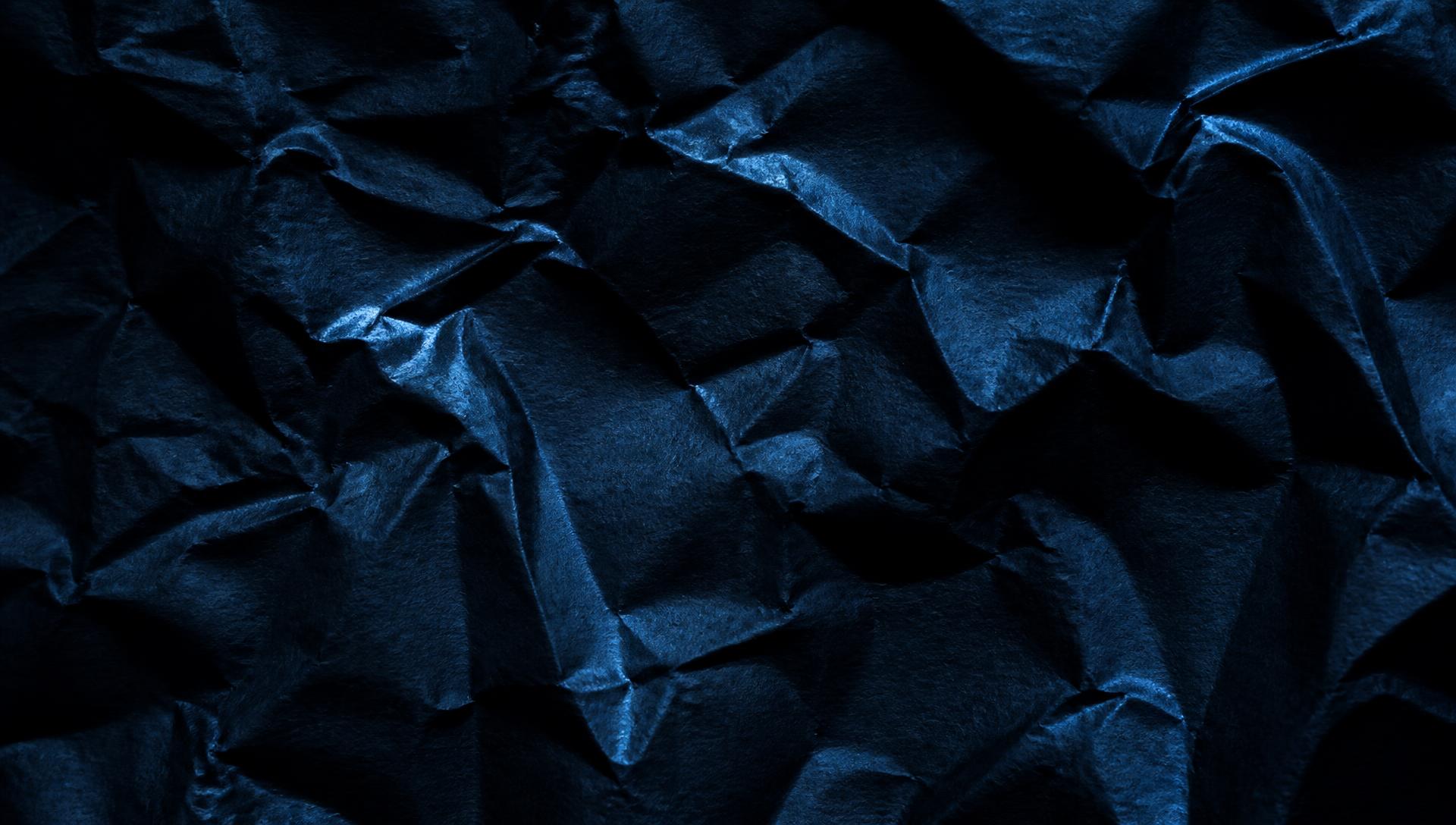 Crumpled navy paper lit by raking light